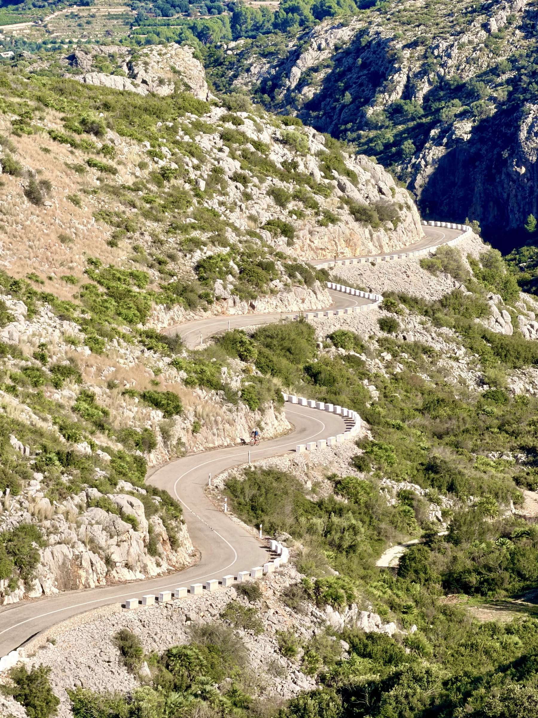 Un cycliste roule seul sur une route sinueuse au pied d’une pente rocheuse sur la Costa Blanca