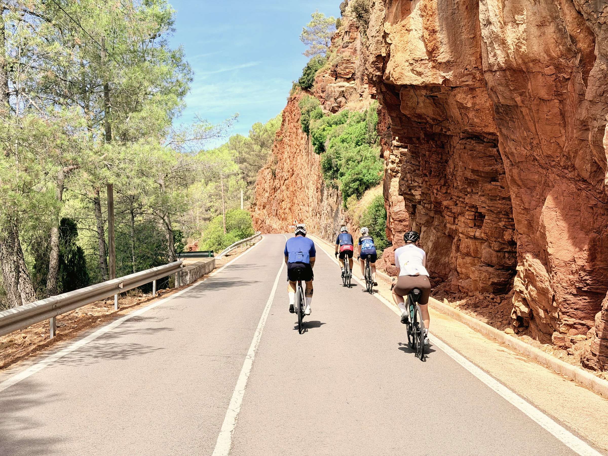 Trois cyclistes sur route traversent une gorge de roches rouges sur la Costa Blanca