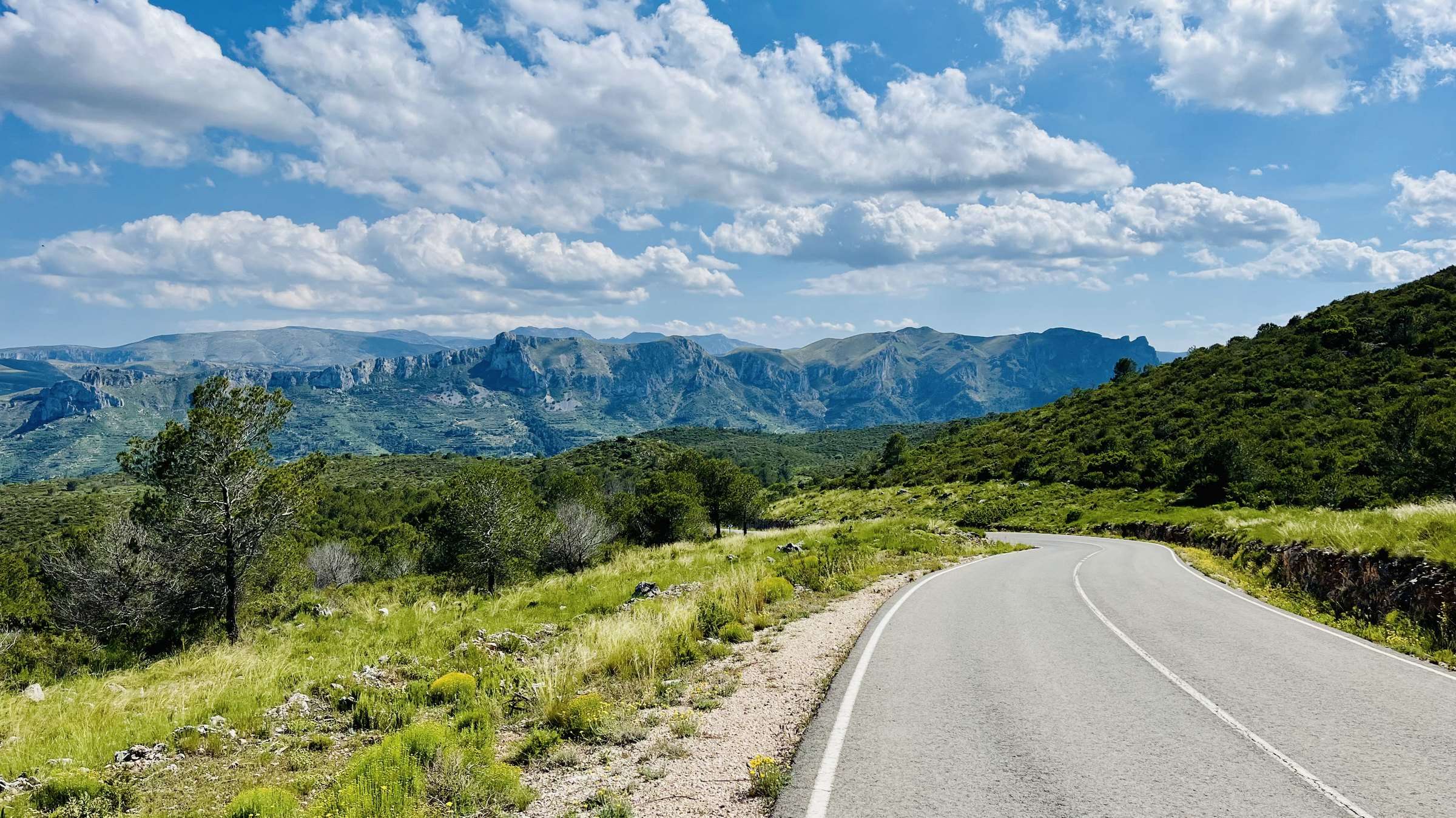 Une route déserte entre des collines vertes, avec une chaîne de montagnes en arrière-plan sur la Costa Blanca
